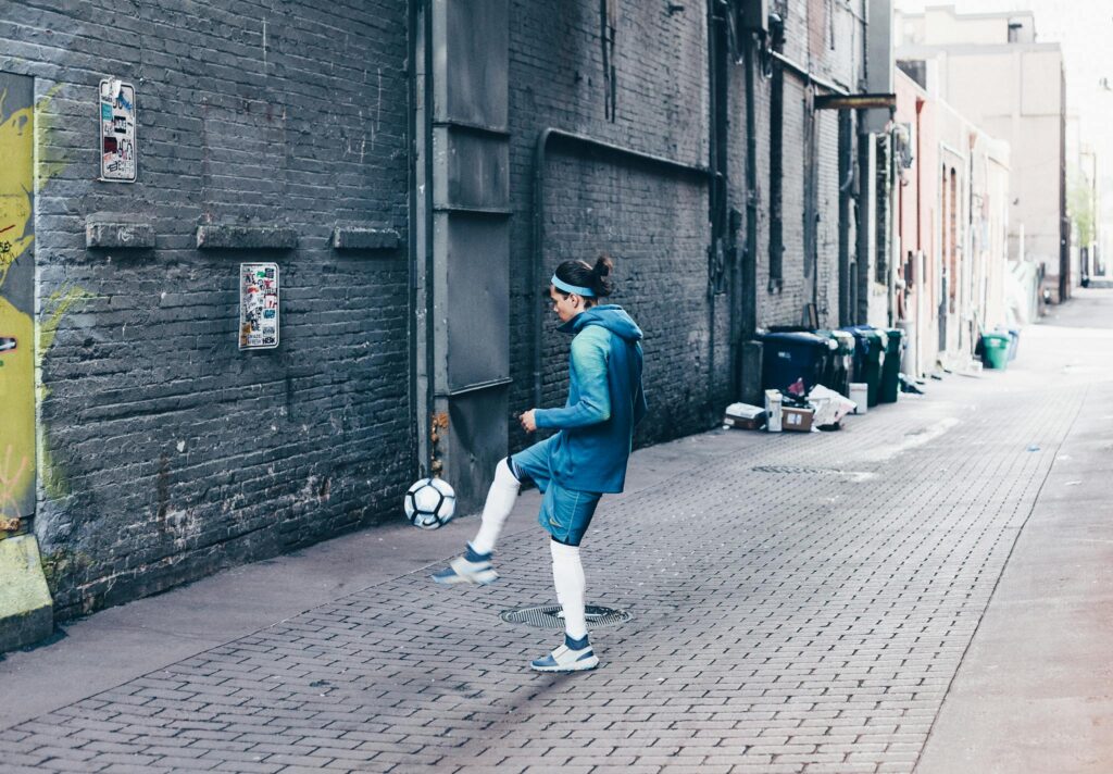 A man practicing soccer in a gritty urban alleyway, highlighting urban sports culture.