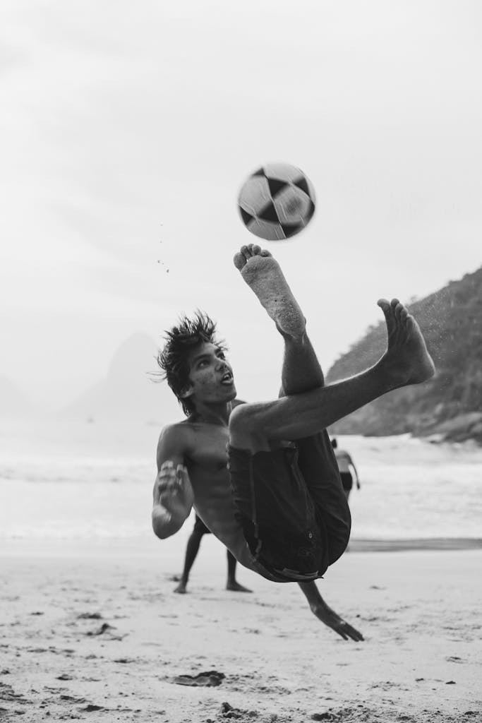 Black and white photo of a man performing a bicycle kick on Rio's beach.